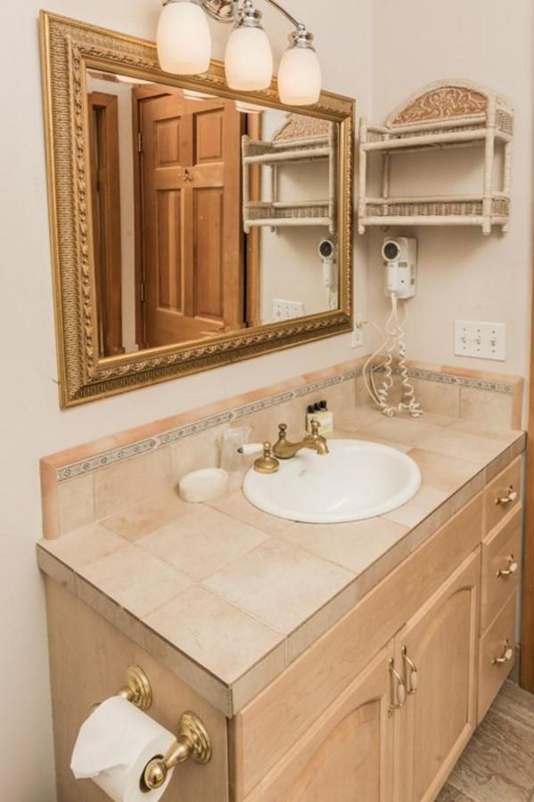 Bathroom vanity with gold-framed mirror, light fixtures, sink, and beige cabinets.