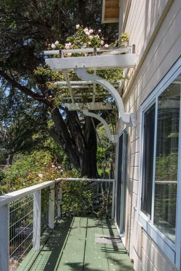 Balcony with white railing and trellis with flowers, attached to a light-colored house.