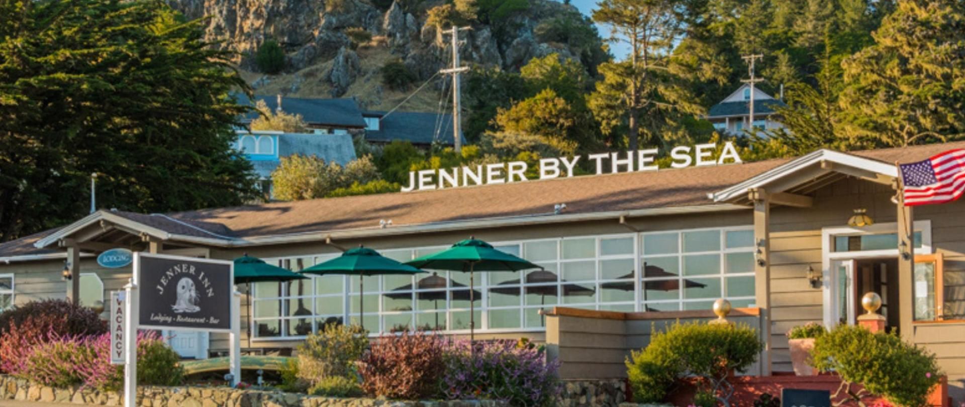 Jenner by the Sea restaurant with green umbrellas, sign, and American flag; coastal setting.