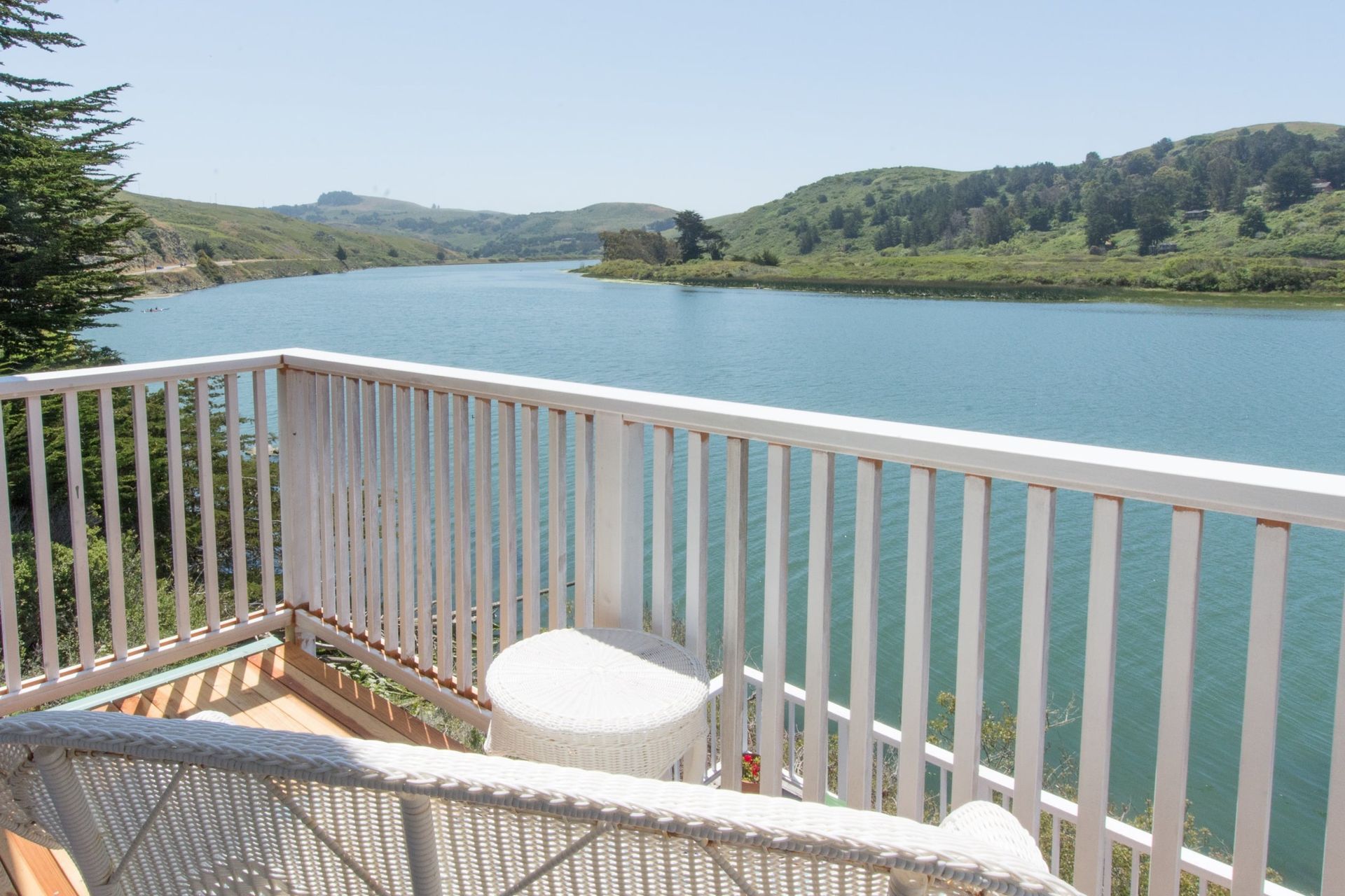 Balcony overlooking a wide, calm body of water with forested hills on the far shore; sunny day.