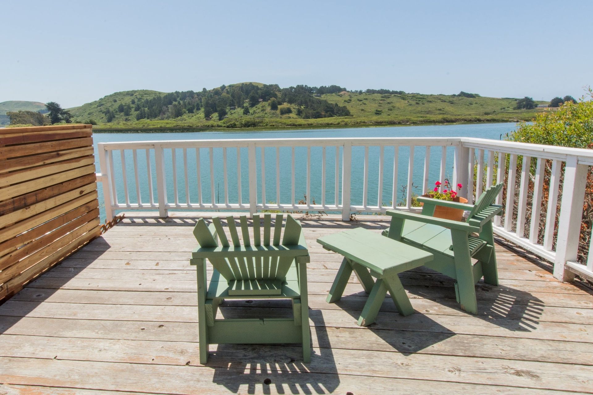 Wooden deck with two green chairs and a small table overlooking a body of water and hills.