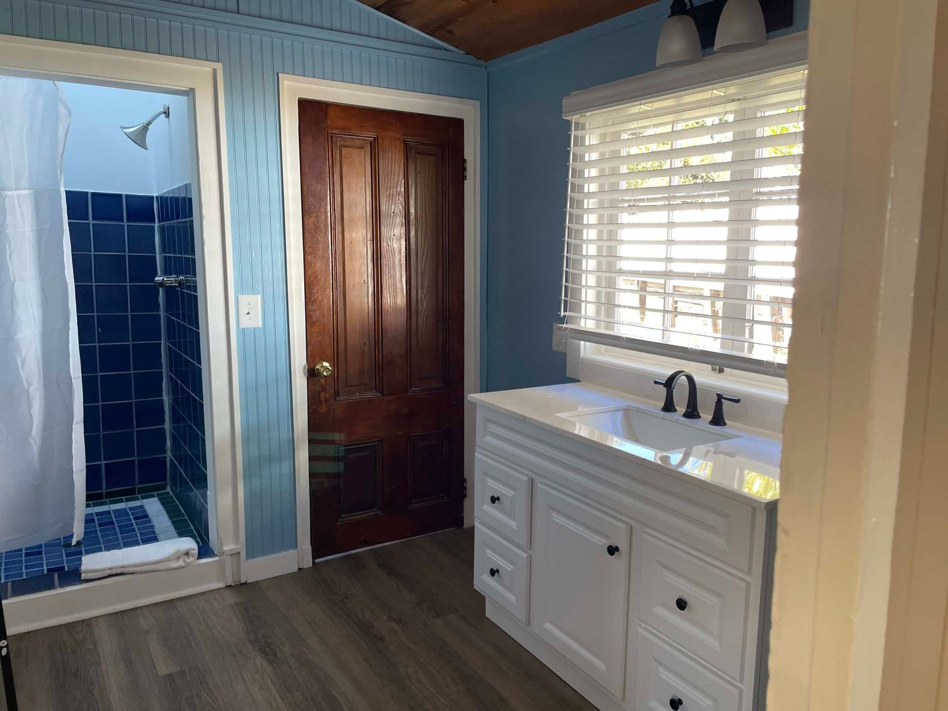 Bathroom with blue walls, white vanity, dark wood door, and a shower.