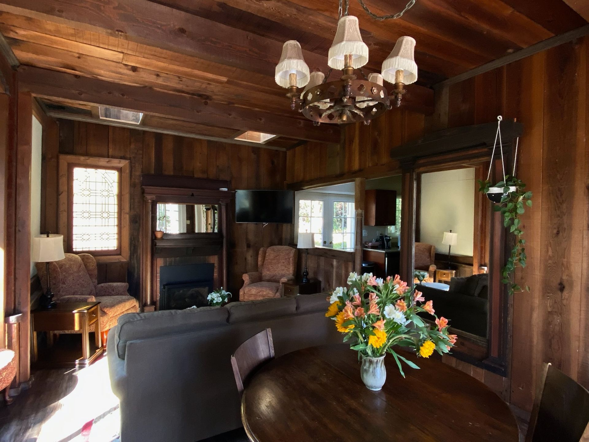 Cozy wood-paneled living room with a sectional sofa, round table with flowers, and a chandelier.
