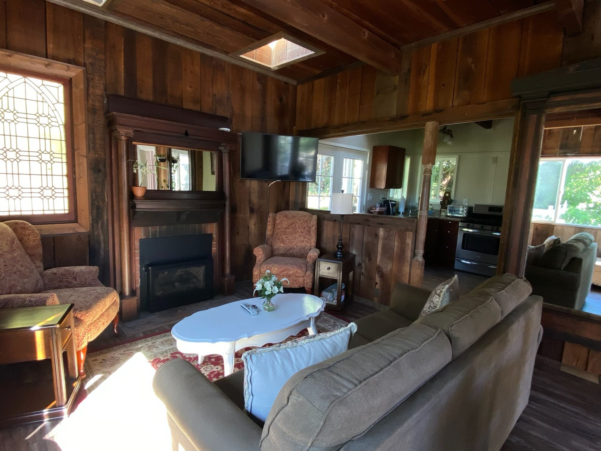 Cozy living room with wood paneling, fireplace, and a small TV. Features include a sofa, chairs, and a white coffee table.