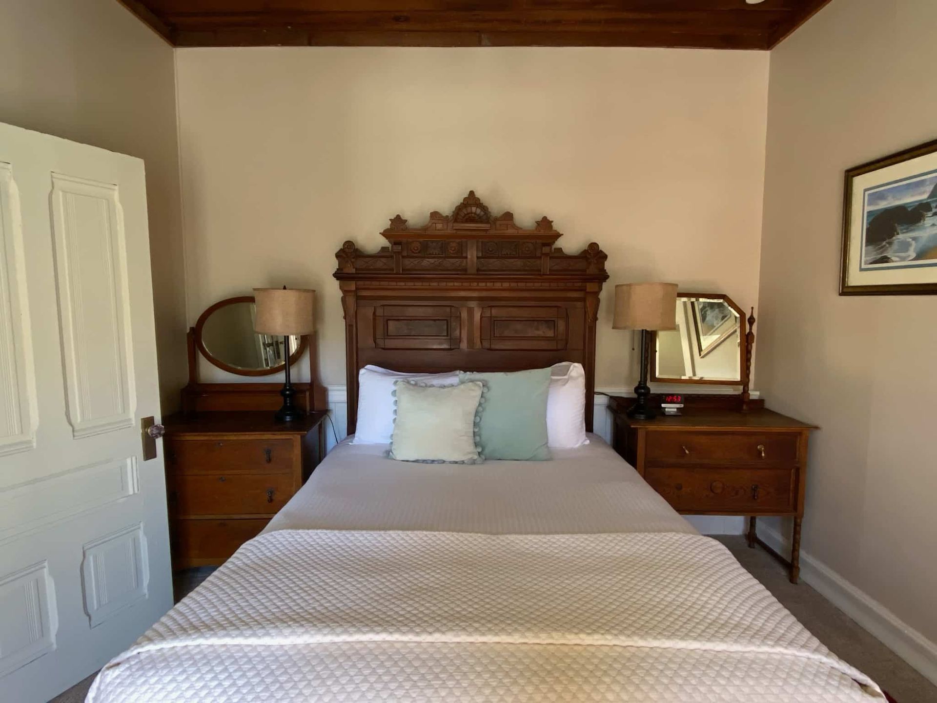 Bedroom with ornate wooden headboard, two nightstands with mirrors, bed with light grey cover.