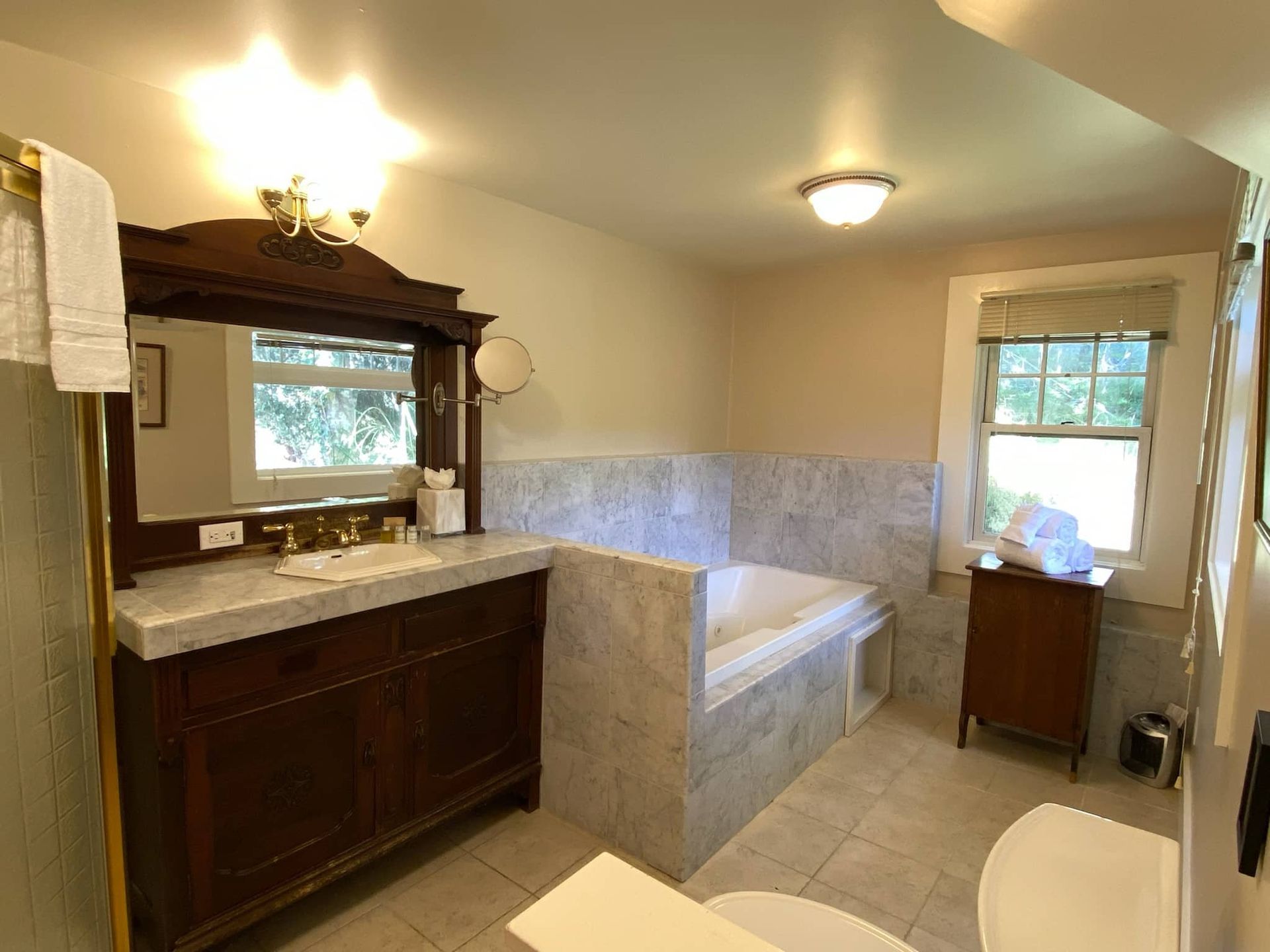 Bathroom with vanity, built-in tub, and window. Marble tiles on floor and walls. Dark wood cabinets and mirror frame.