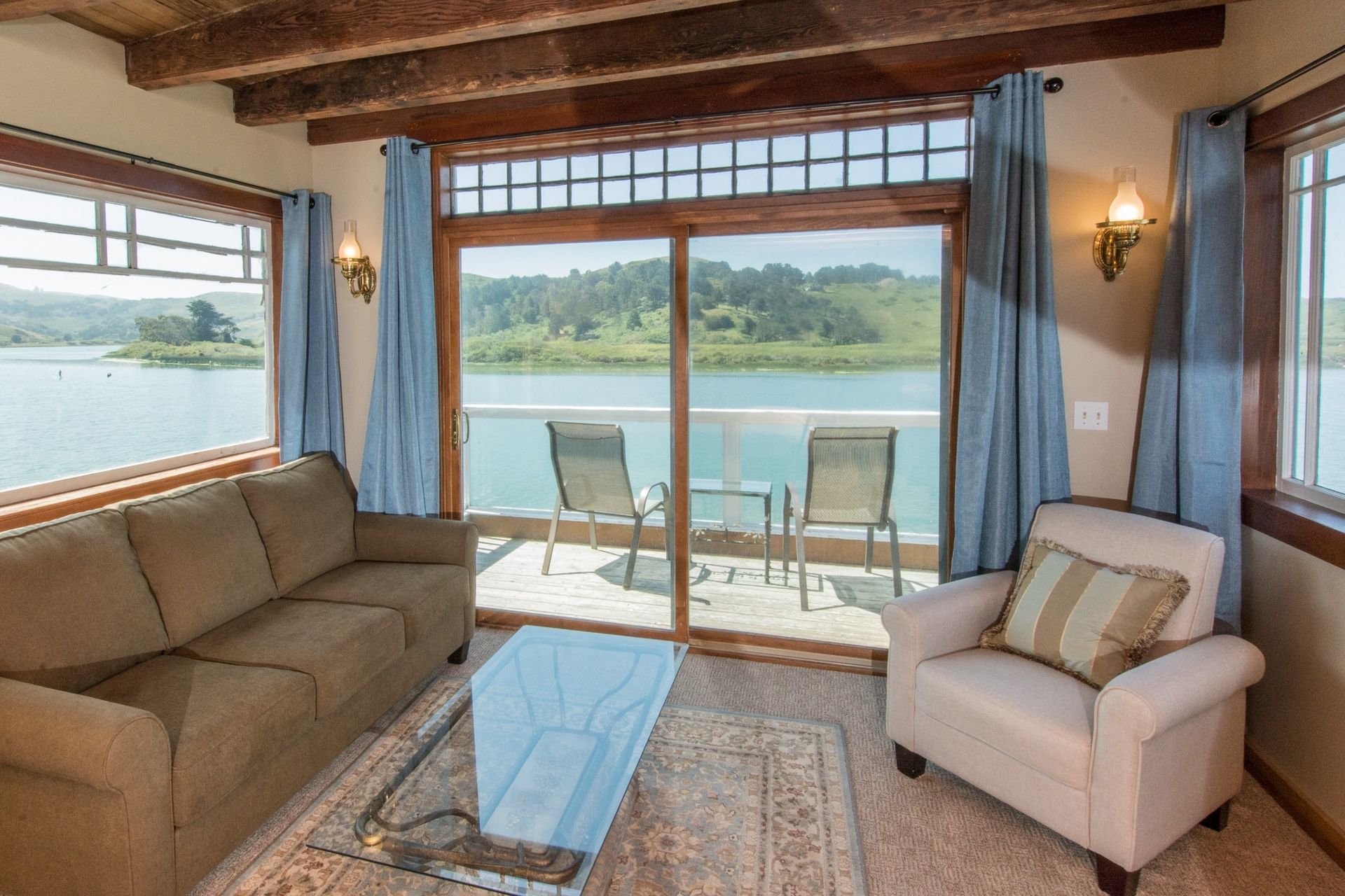 Living room with water view, beige couch and armchair, sliding door to balcony, blue curtains.