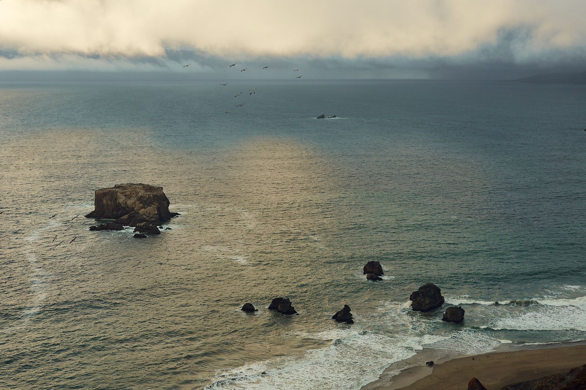 Ocean with rocky outcroppings, a cloudy sky, and a sandy beach.