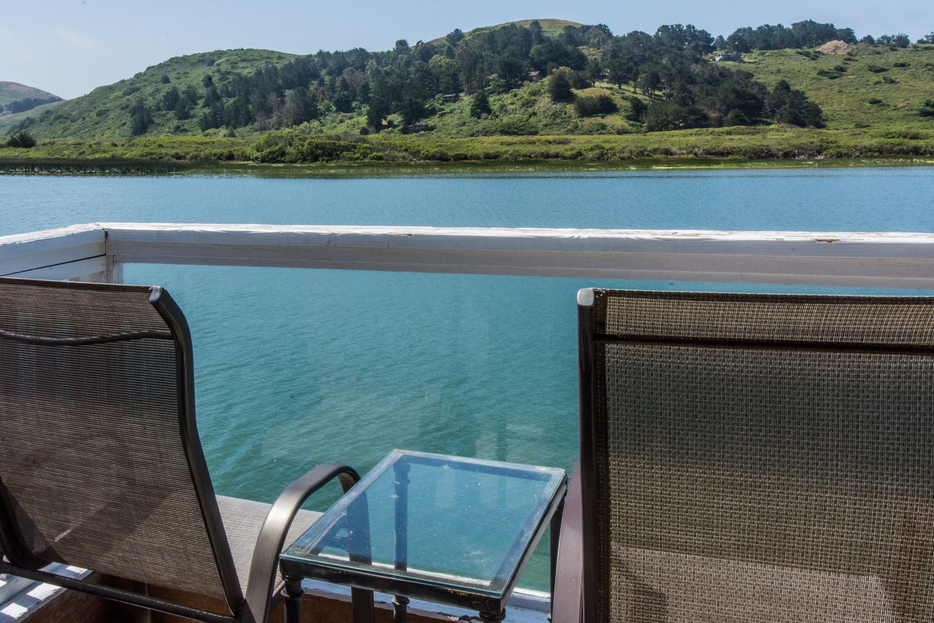 Two lounge chairs and a small table on a deck overlooking a lake and forested hills.