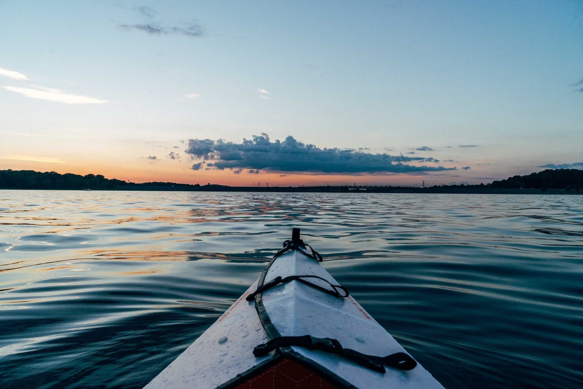 Kayak on calm water at sunset; orange and blue sky reflected.