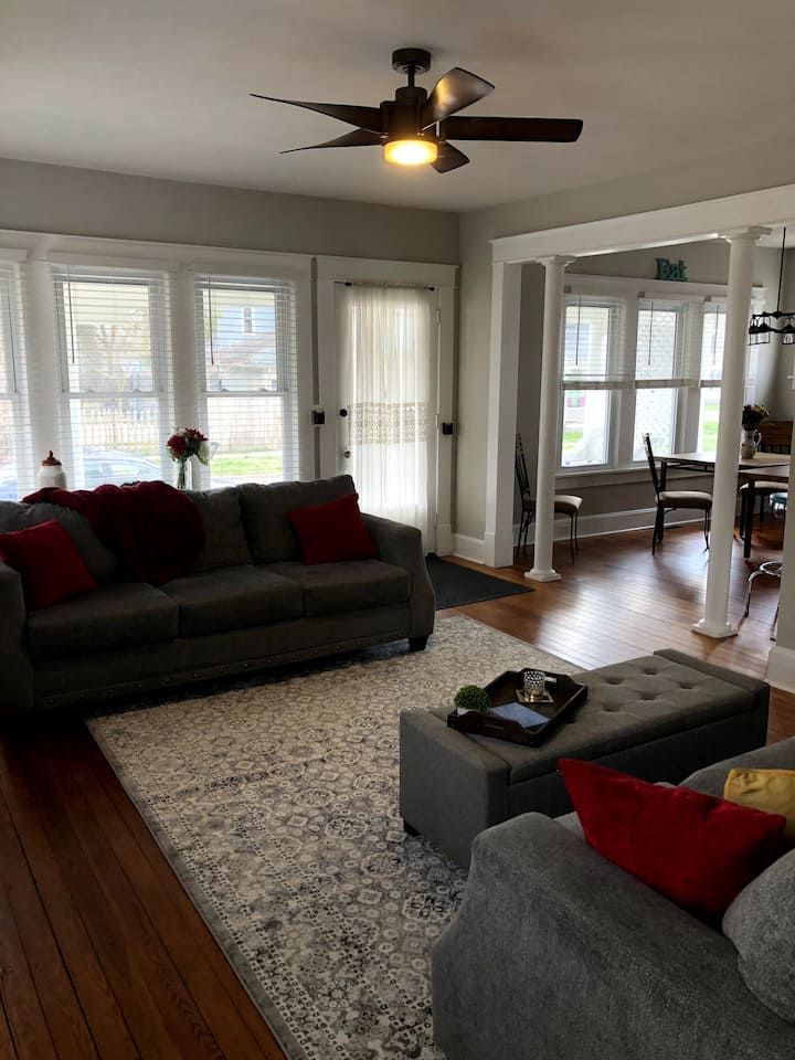 A living room with a couch , chair , ottoman and ceiling fan.
