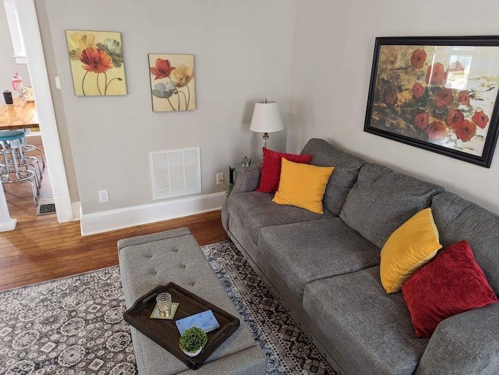 A living room with a couch , ottoman , coffee table and paintings on the wall.