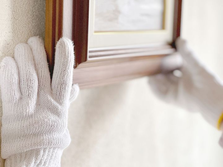A person wearing white gloves is holding a picture frame on a wall.