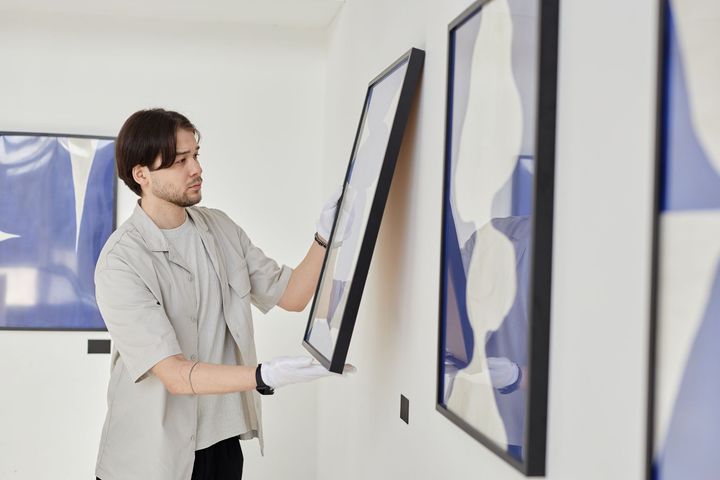 A man is hanging a picture on a wall in a museum.