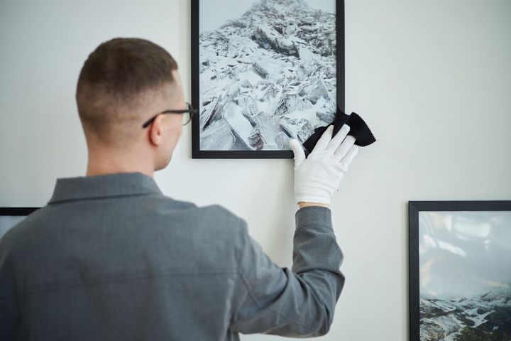 A man wearing white gloves is hanging a picture on a wall.