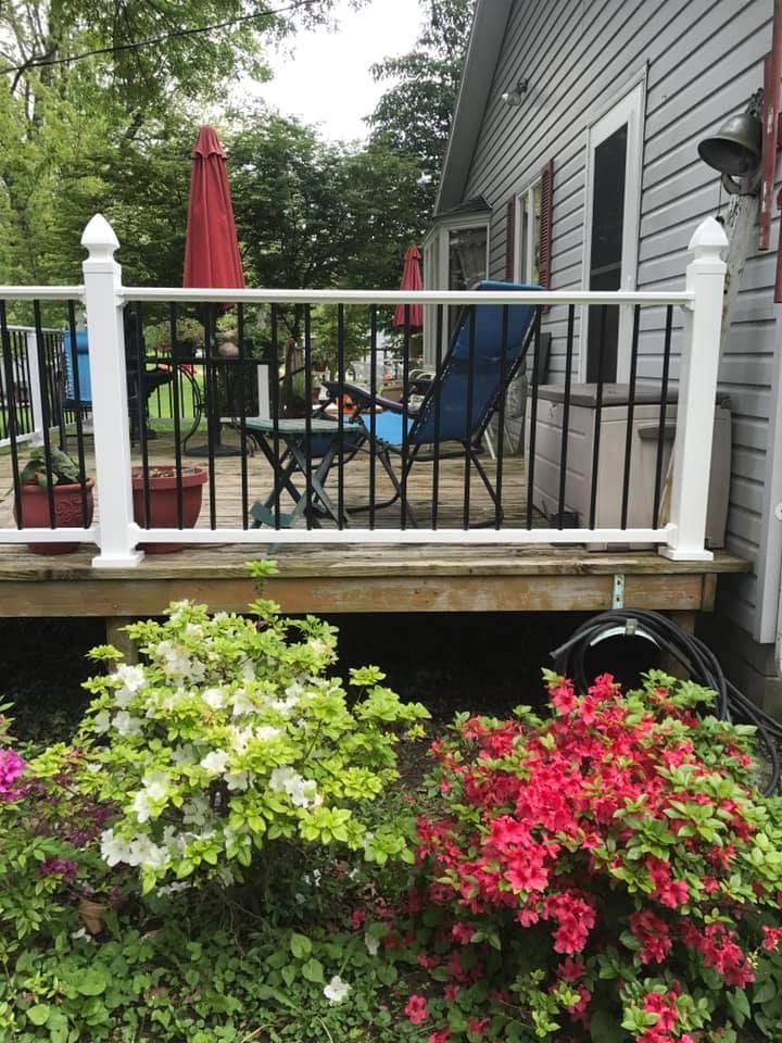A white porch railing with black balusters sits in front of a house, above bushes with white and pink azalea flowers.