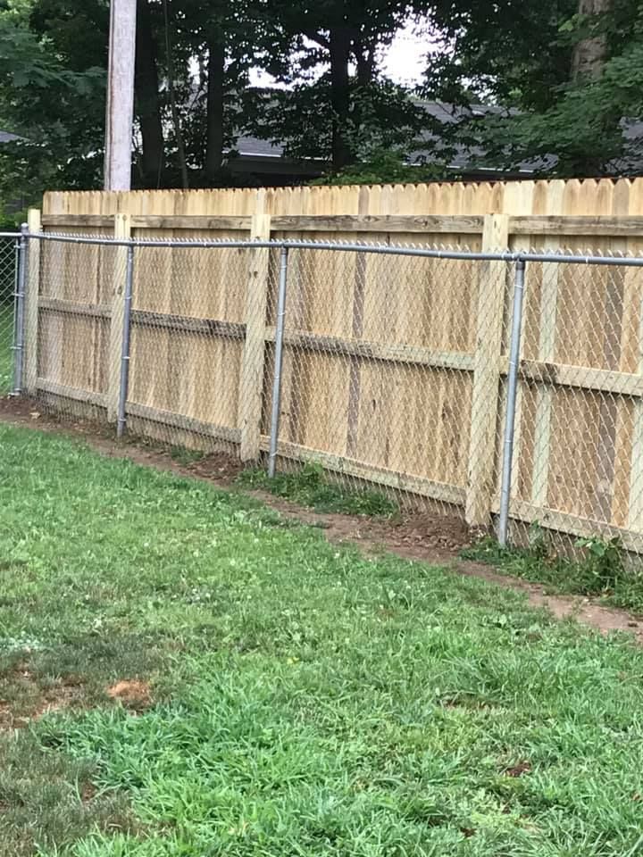 A wooden privacy fence installed in front of an existing chain-link fence on a grassy lawn.