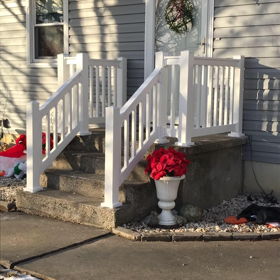 Front concrete steps with white vinyl railings and a white urn planter holding bright red artificial flowers.