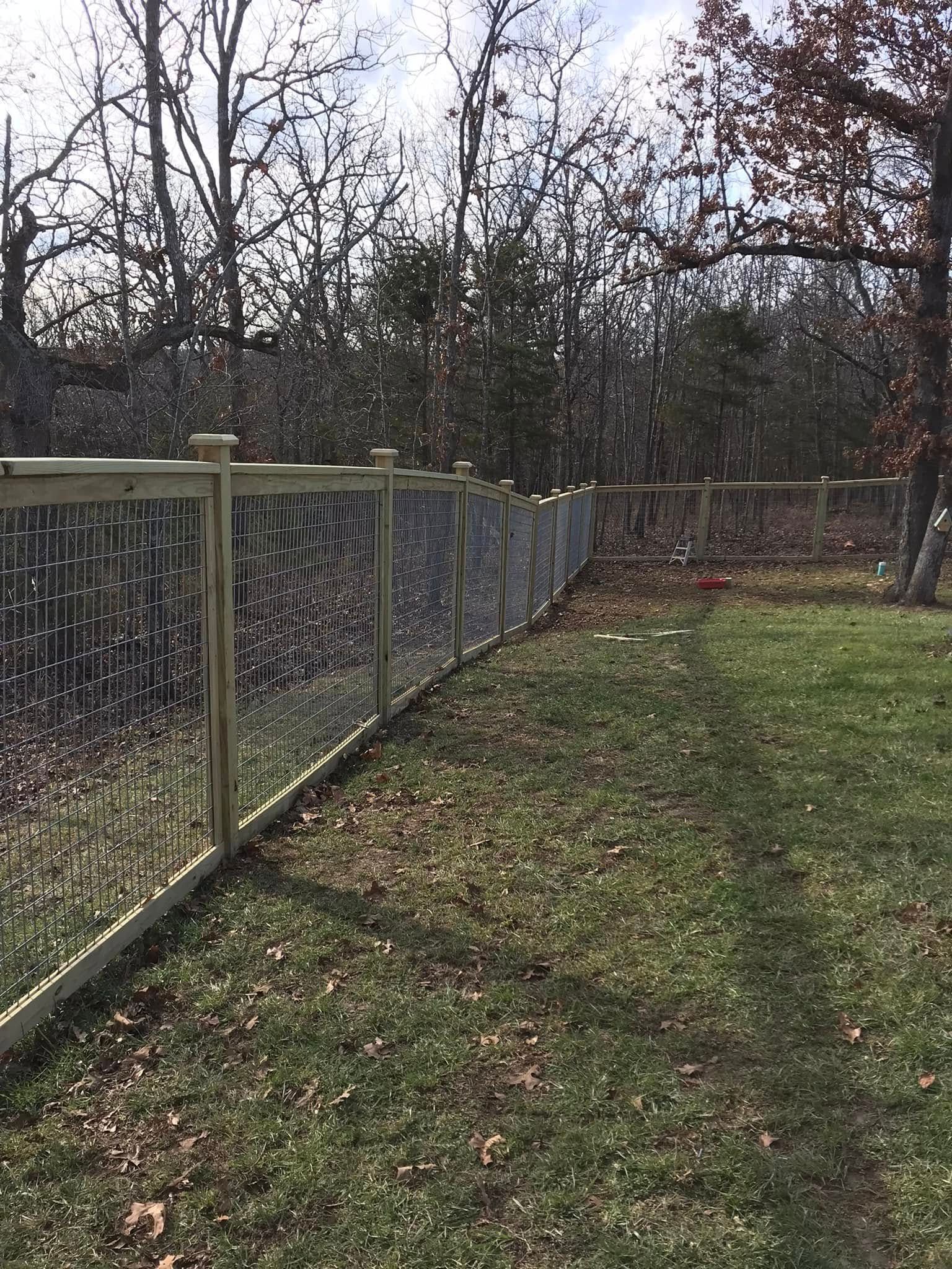 A newly installed wooden fence with wire mesh panels bordering a grassy lawn and a wooded area.