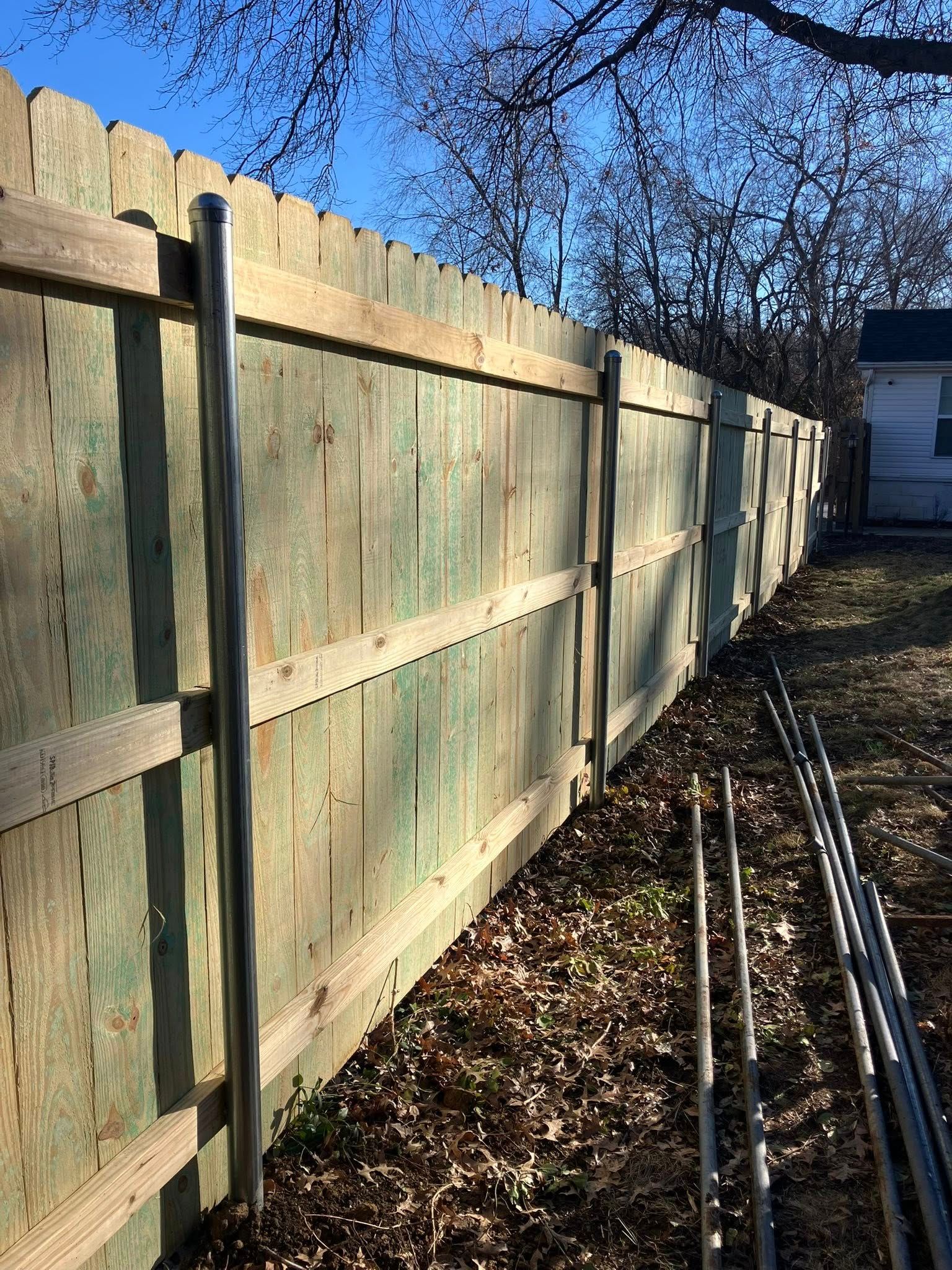 A wooden privacy fence under a clear blue sky, featuring vertical metal support posts along the exterior.