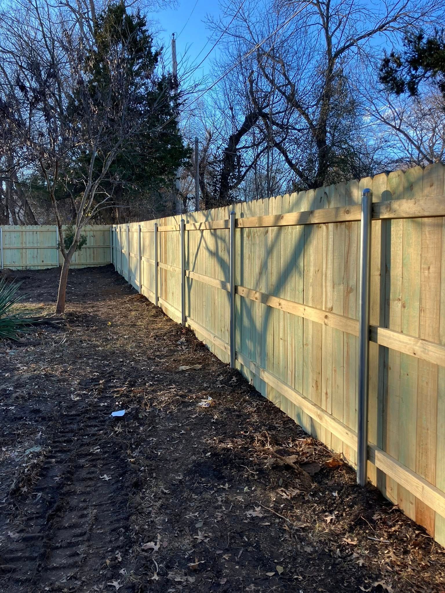 A wooden privacy fence with metal support posts, seen from the side in an outdoor yard with scattered fallen leaves.