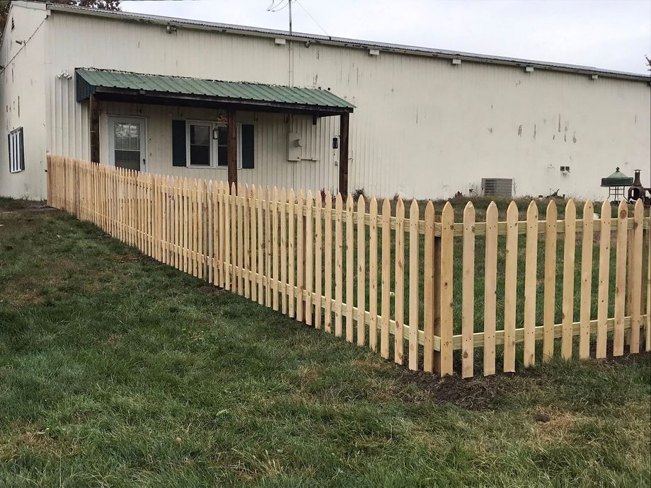 A newly installed wooden picket fence curves in front of a white building with a small green-roofed entryway.