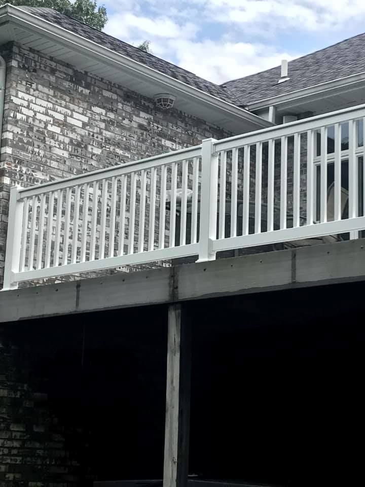 White deck railing with vertical balusters mounted on a home deck against a brick wall.
