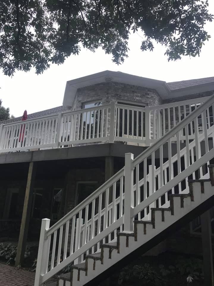 A stone-walled house with a raised wooden deck and a white-railed staircase leading to the ground level.