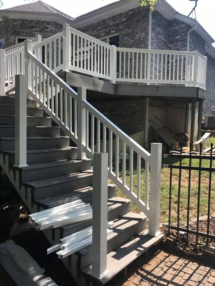 A wooden staircase with white railings leading up to a deck attached to a brick house.