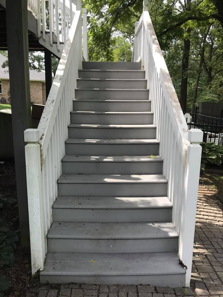 Gray wooden stairs leading up to an elevated deck with white railings in an outdoor setting.