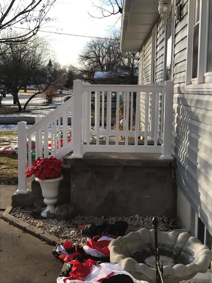 White porch railing on a stone-faced stoop next to a house, with a potted plant and scattered decorations below.
