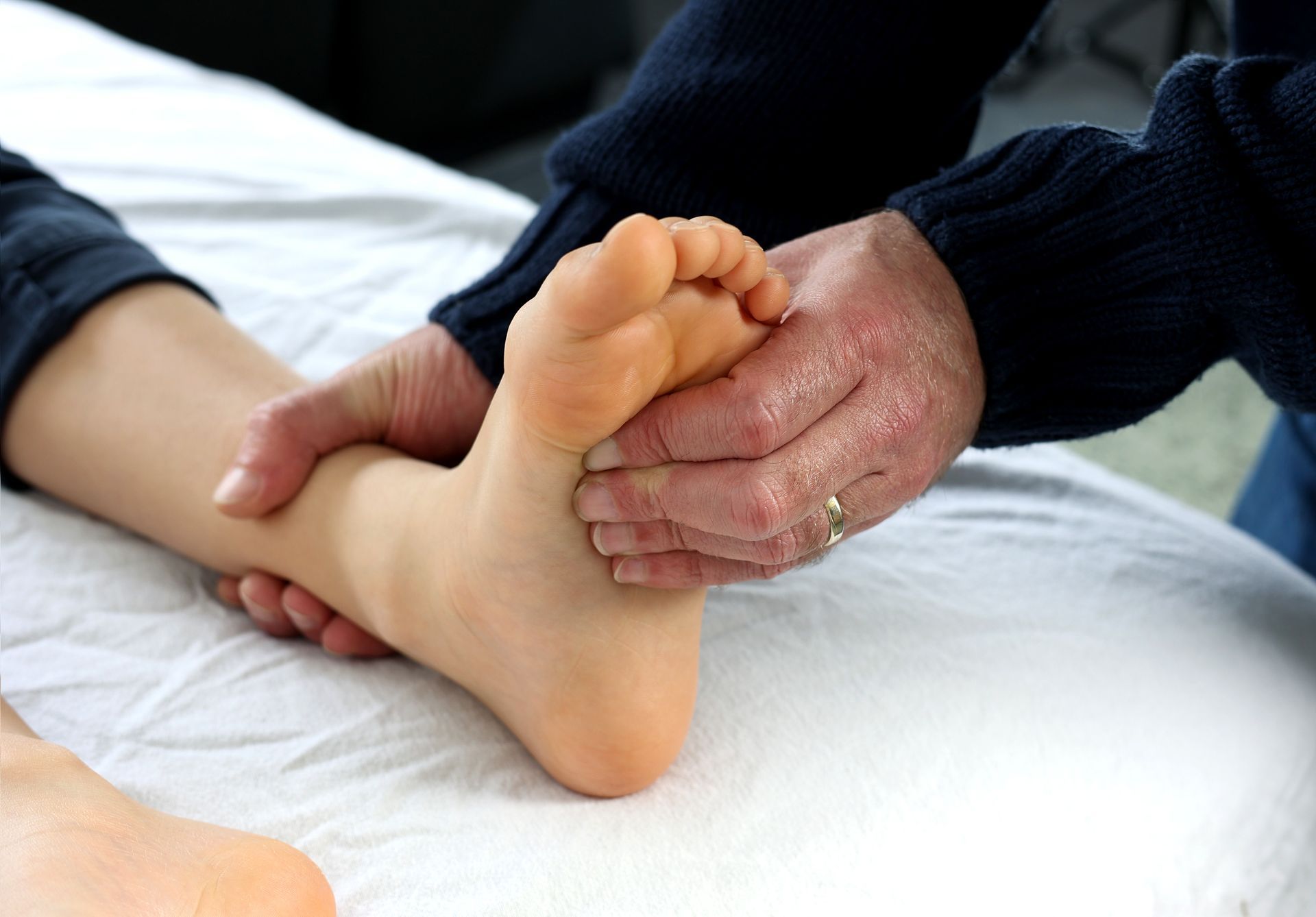 A Person is Giving a Child a Foot Massage on a Bed — Newcastle Foot & Ankle Clinic Charlestown In Charlestown, NSW