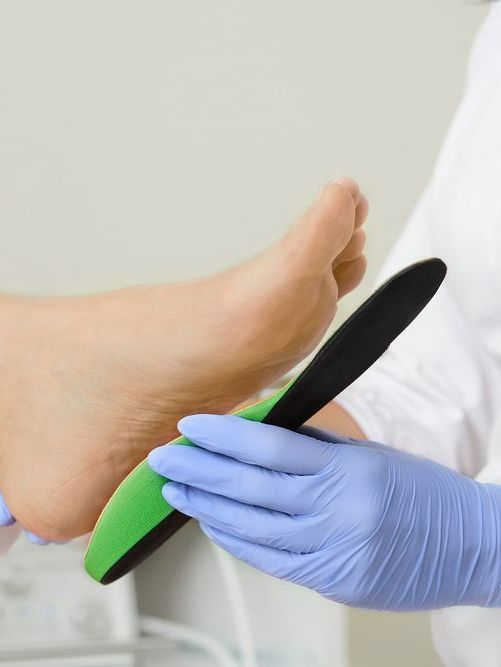 A Person Wearing Blue Gloves is Holding a Green Insole — Newcastle Foot & Ankle Clinic Charlestown In Charlestown, NSW