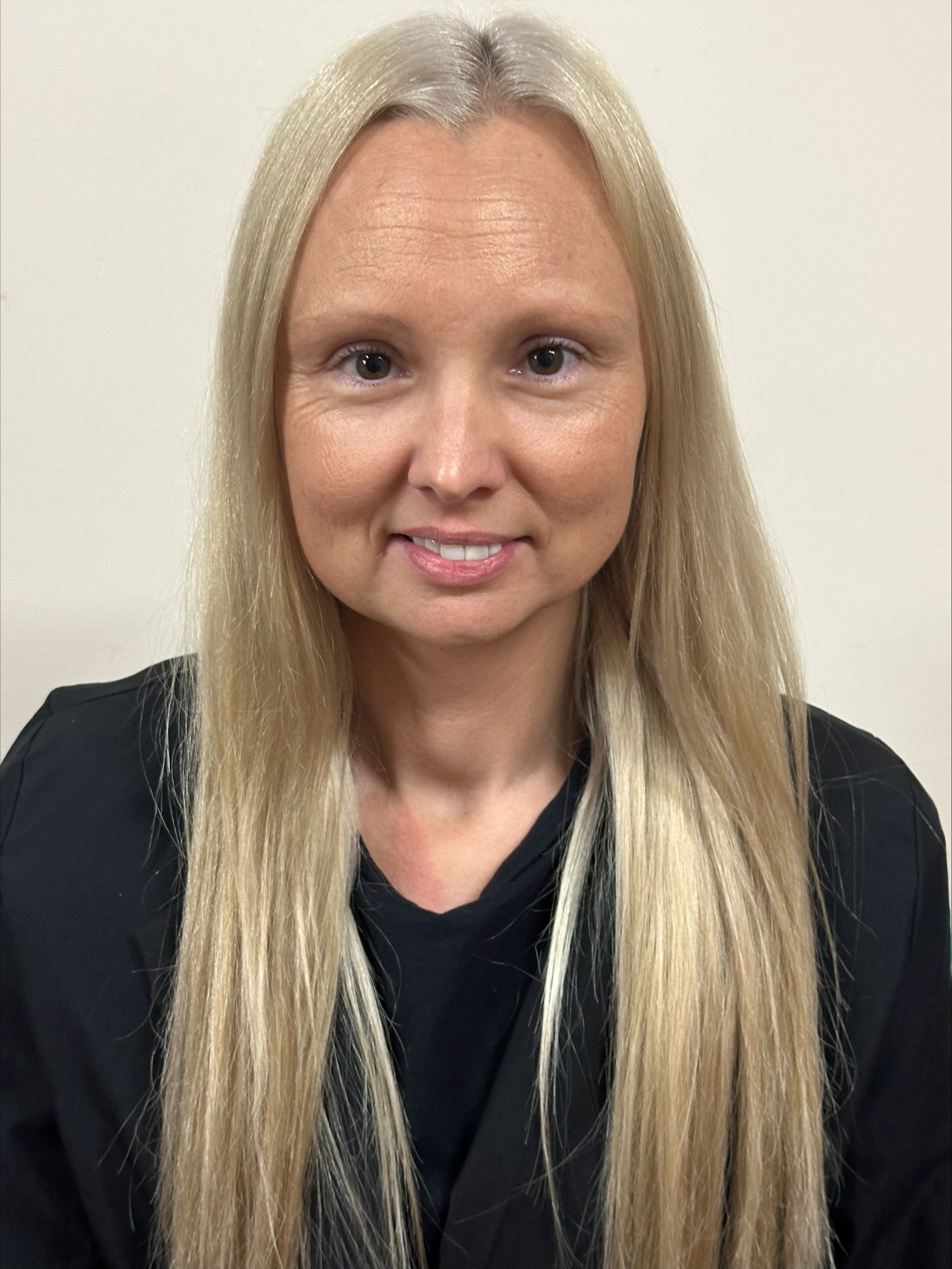 A woman with long blonde hair is wearing a black shirt and smiling for the camera.