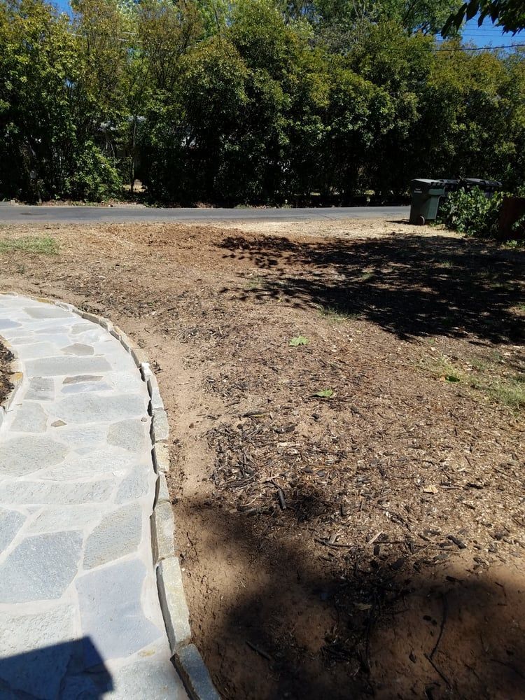 A stone walkway leading to a dirt field next to a road.
