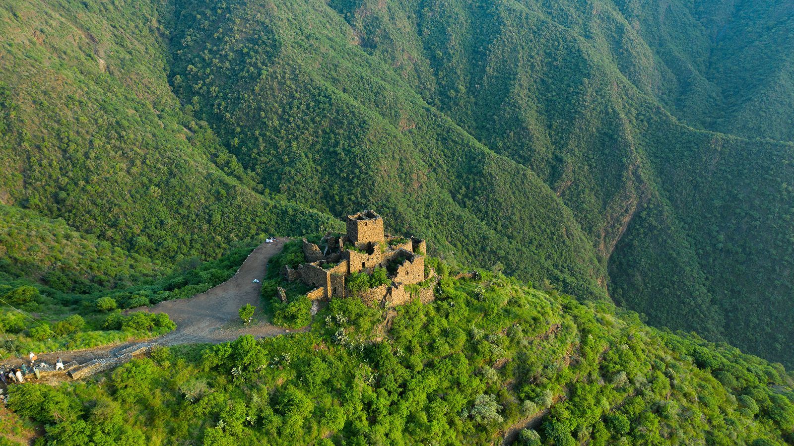 Stone fortress atop a green mountain; a path leads up to it.