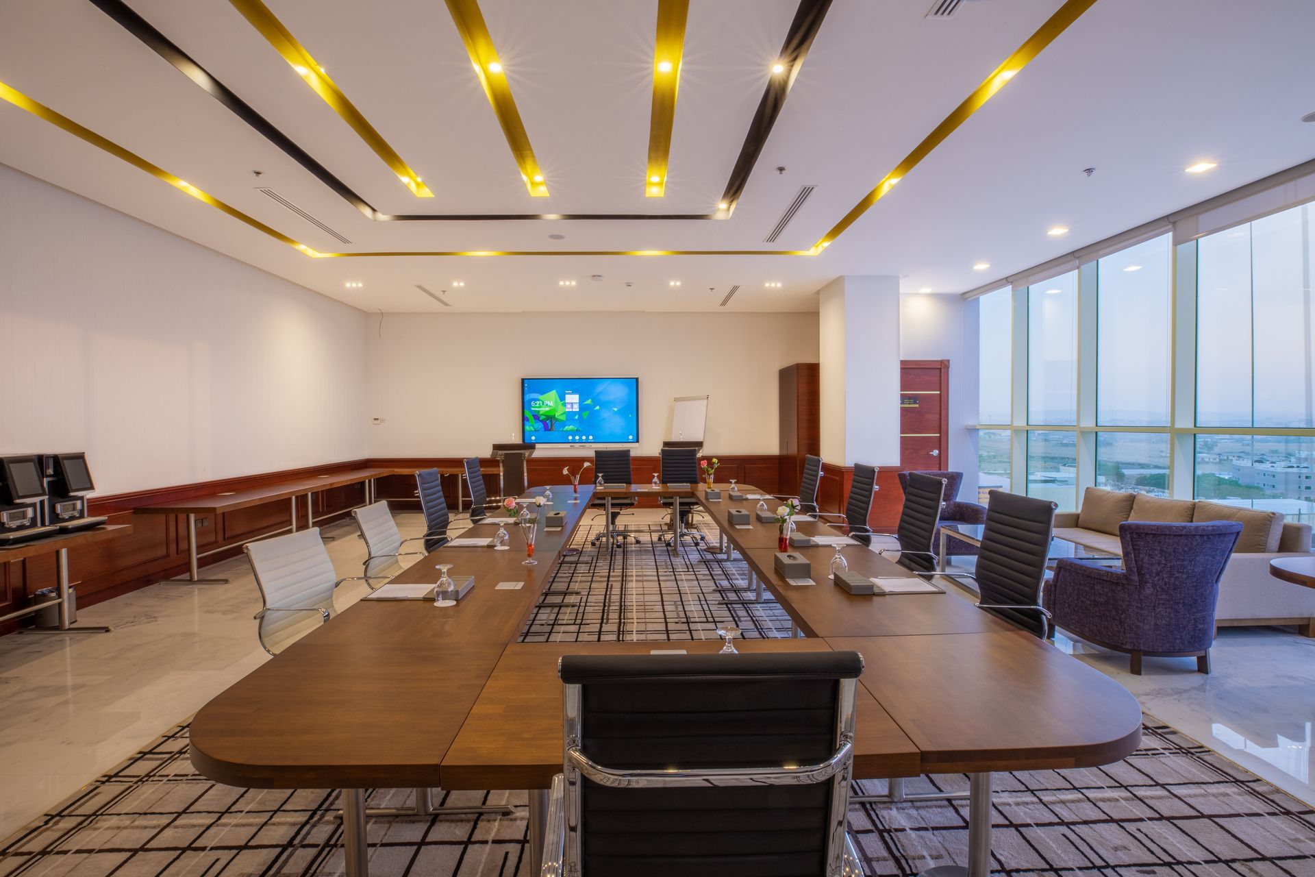 Conference room with large table, chairs, screen, windows, and light fixtures.