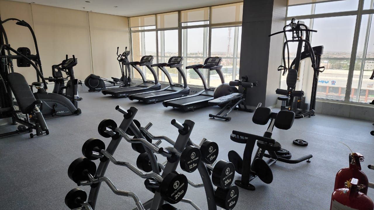 Gym with exercise equipment, including treadmills, weights, and weight machines, near a large window.