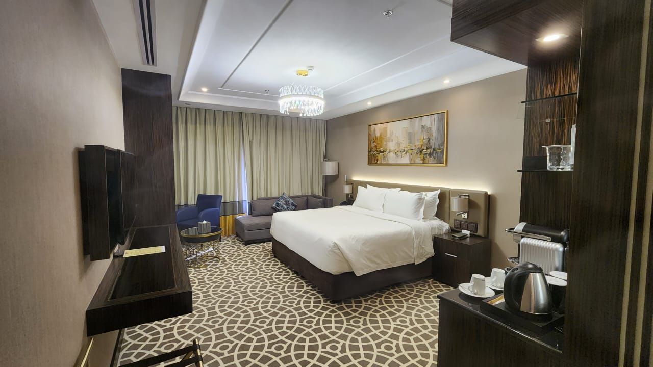 Hotel room with a bed, couch, and a TV. Neutral colors, modern design.