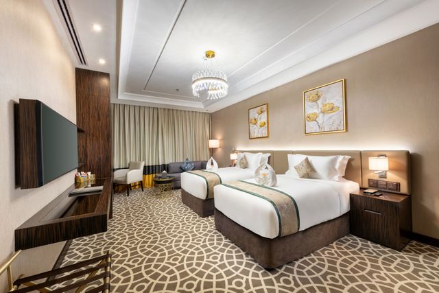 Modern hotel room with two beds, chandelier, patterned carpet, and beige curtains