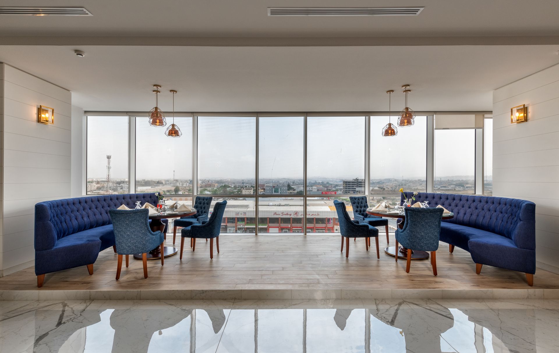 Restaurant with blue booths, tables, and chairs, large windows with city view, light wood floors.