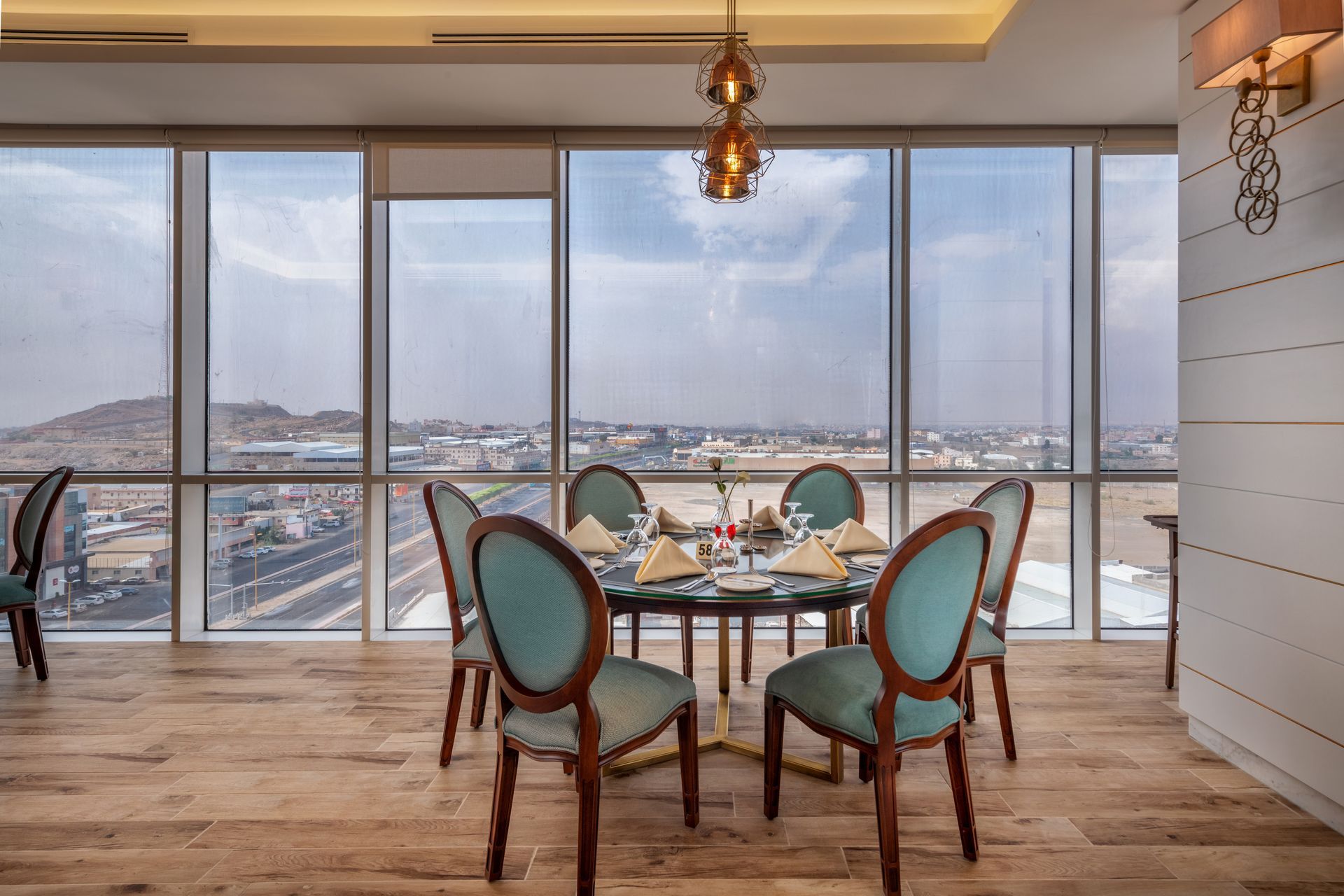 Dining room with round table set for a meal, blue chairs, large windows, city view.