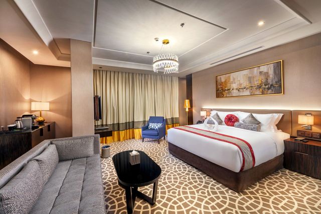 Luxurious hotel room with king bed, sofa, chandelier, and city view through curtains