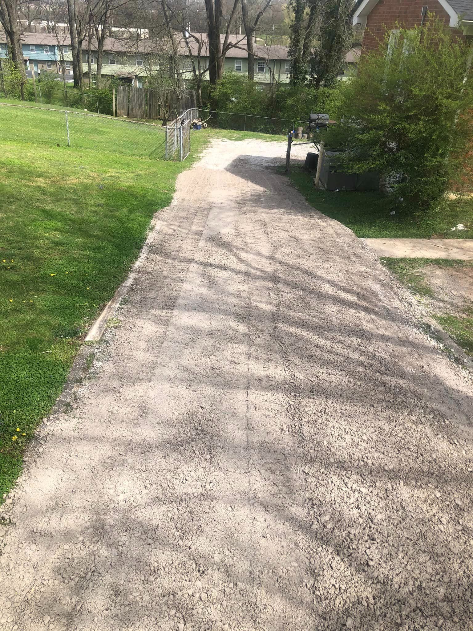 A dirt road going through a grassy area next to a house.