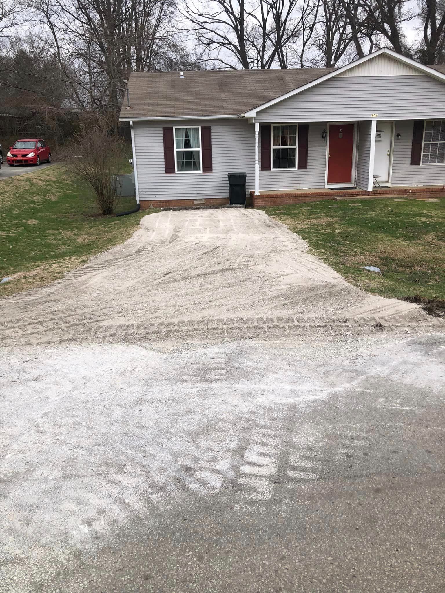 A white house with a red door and a gravel driveway in front of it.