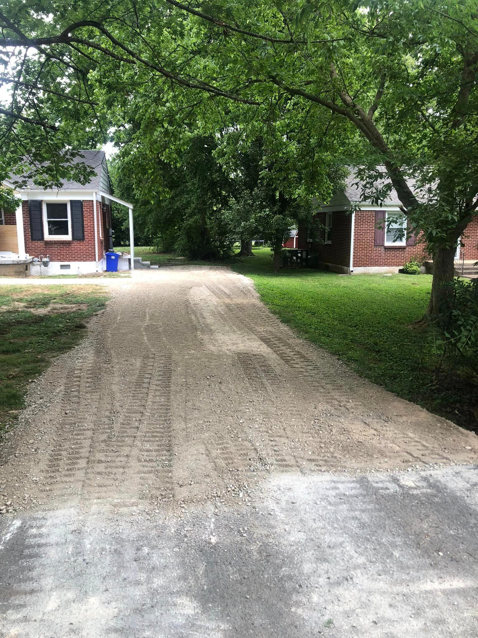 A dirt road leading to a brick house surrounded by trees.