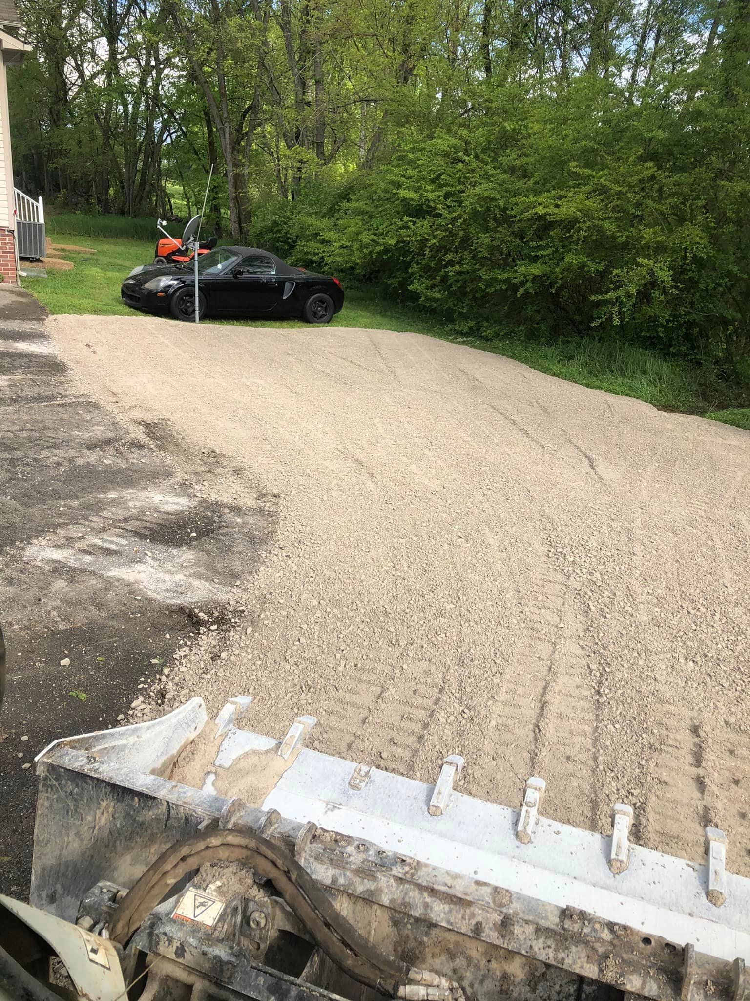 A black car is parked in a gravel driveway next to a tractor.