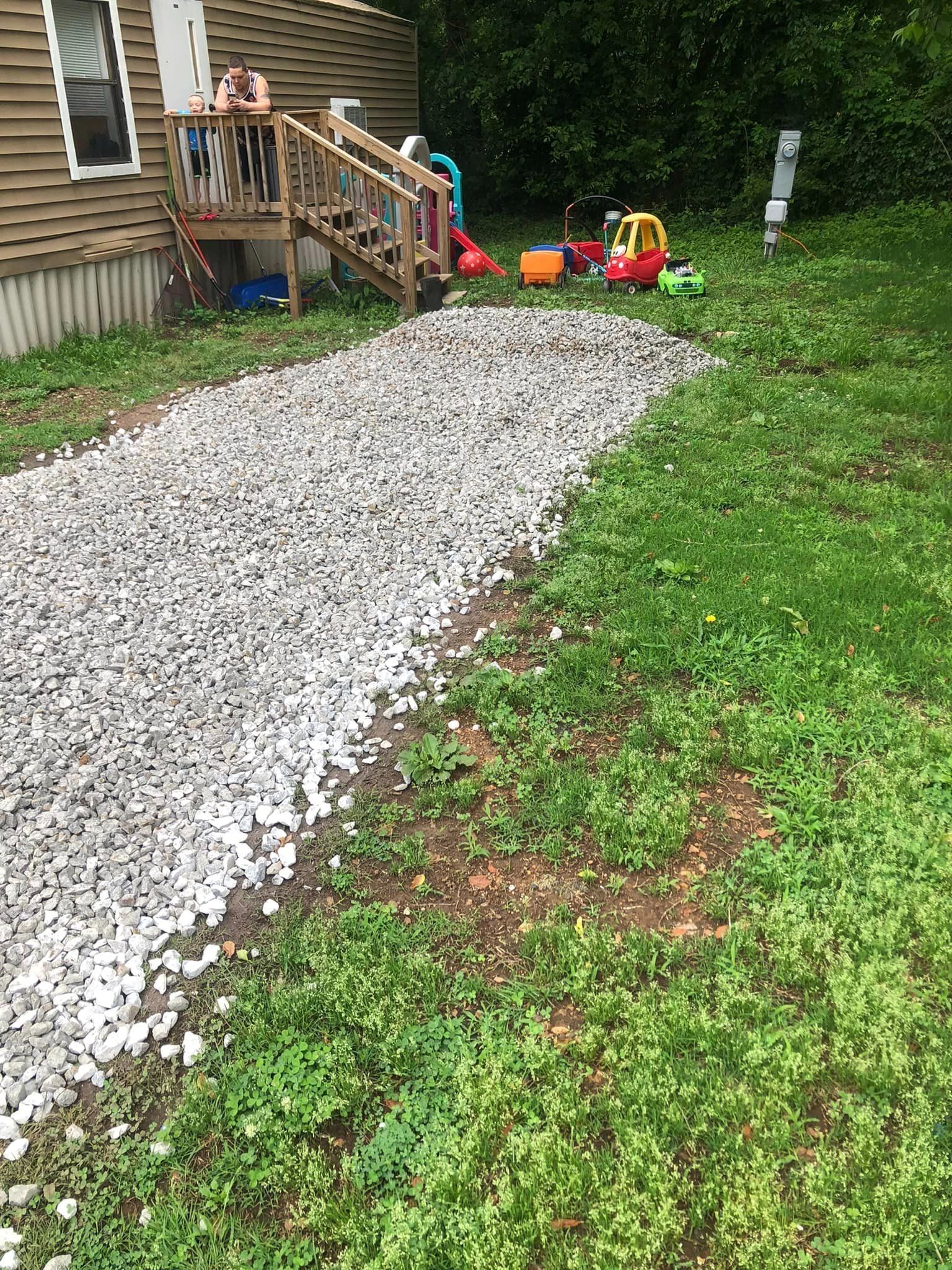 A gravel driveway leading to a house with toys in the grass.