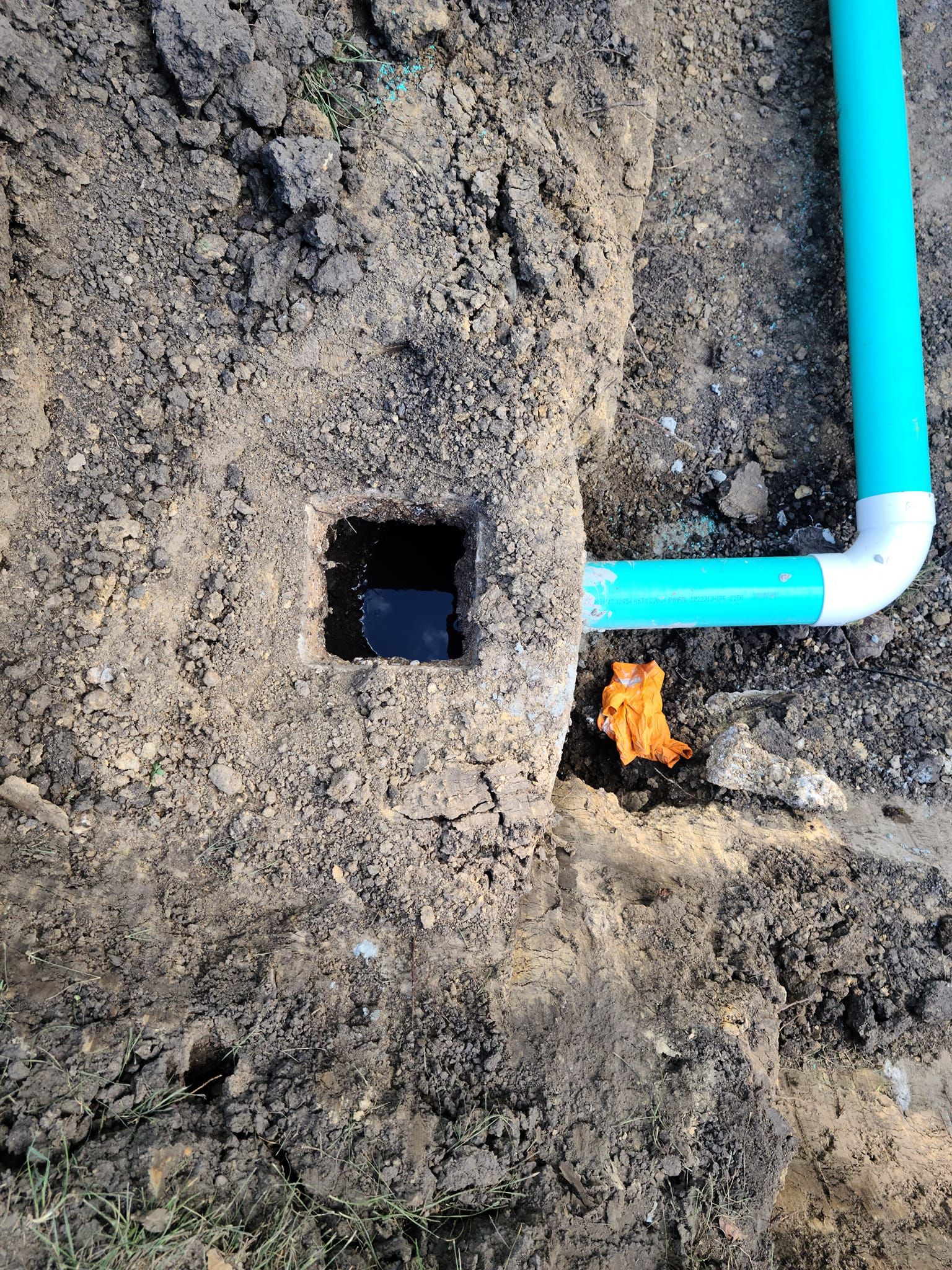 A blue pipe is sitting in the dirt next to a hole in the ground.