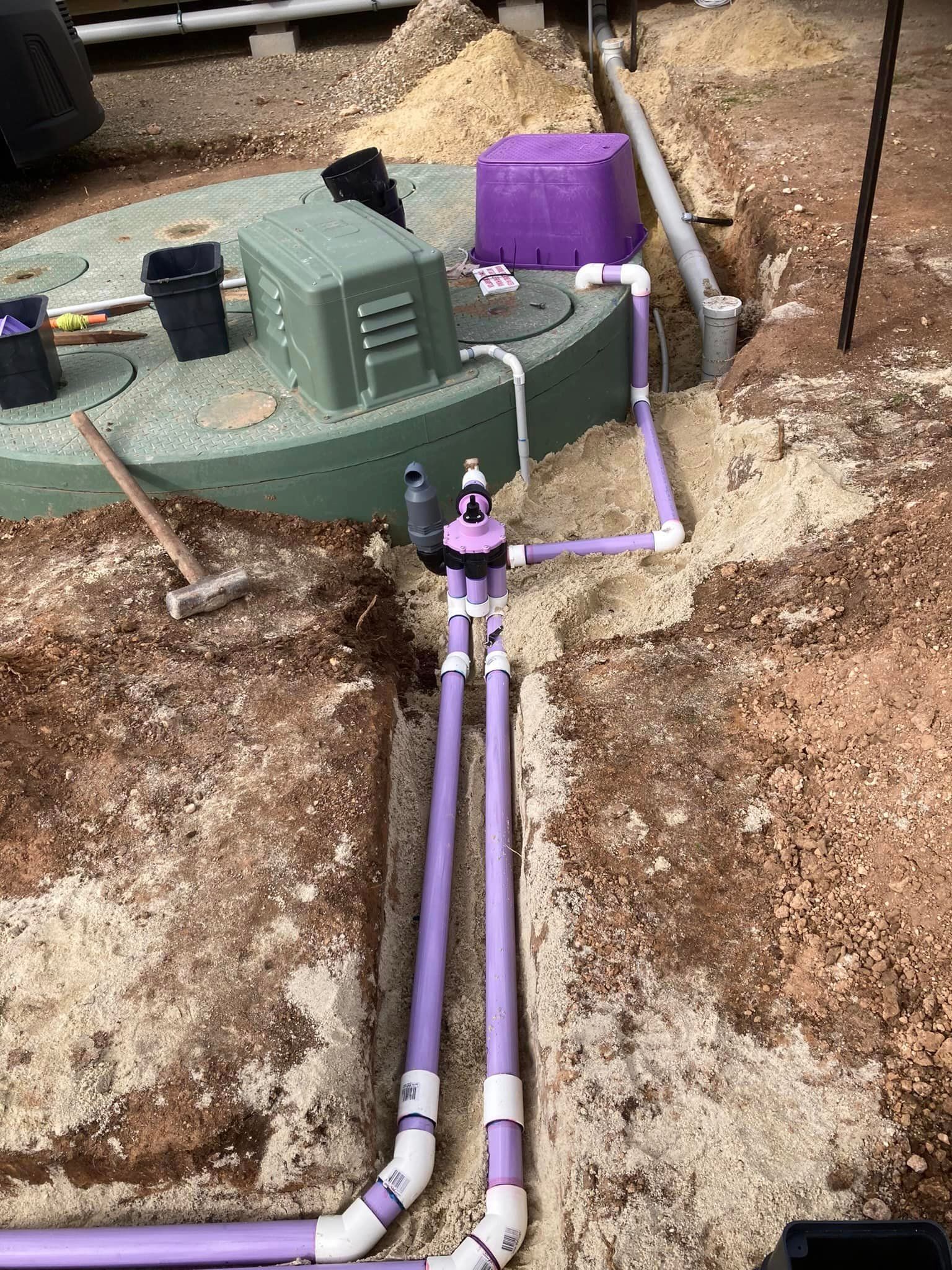 A septic tank is being installed in the dirt with purple pipes.